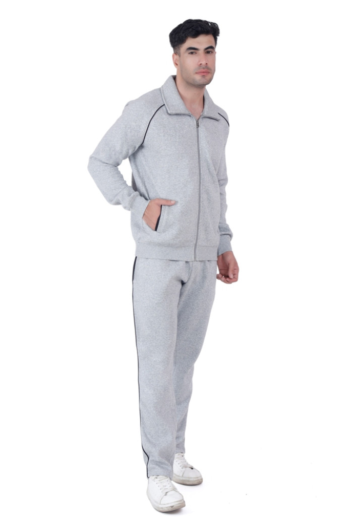 A man wearing Trufit’s Grey Grindle tracksuit with a front zipper and black piping, standing in a casual pose with one hand in the pocket and the other relaxed, paired with white sneakers against a white background.